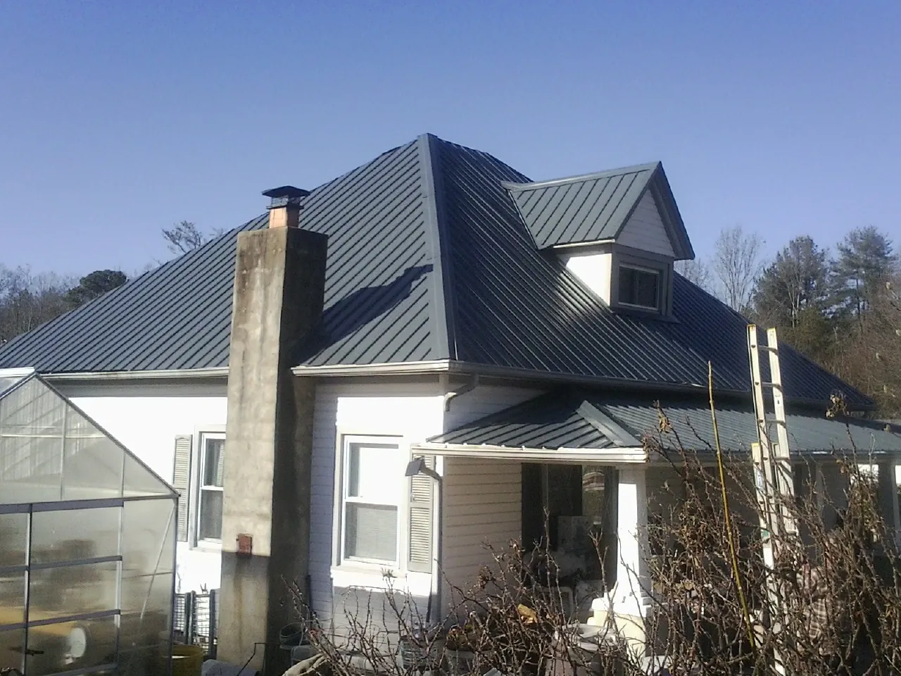 Dark blue standing seam metal roof on a white farmhouse with dormer — Slate & Tile Roof Repair by Roofing Brothers in Whiteland