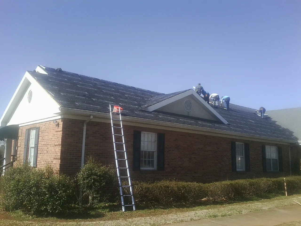Crew tearing shingles off a brick ranch roof with a ladder set — Emergency Roof Repair work by our crew in Whiteland