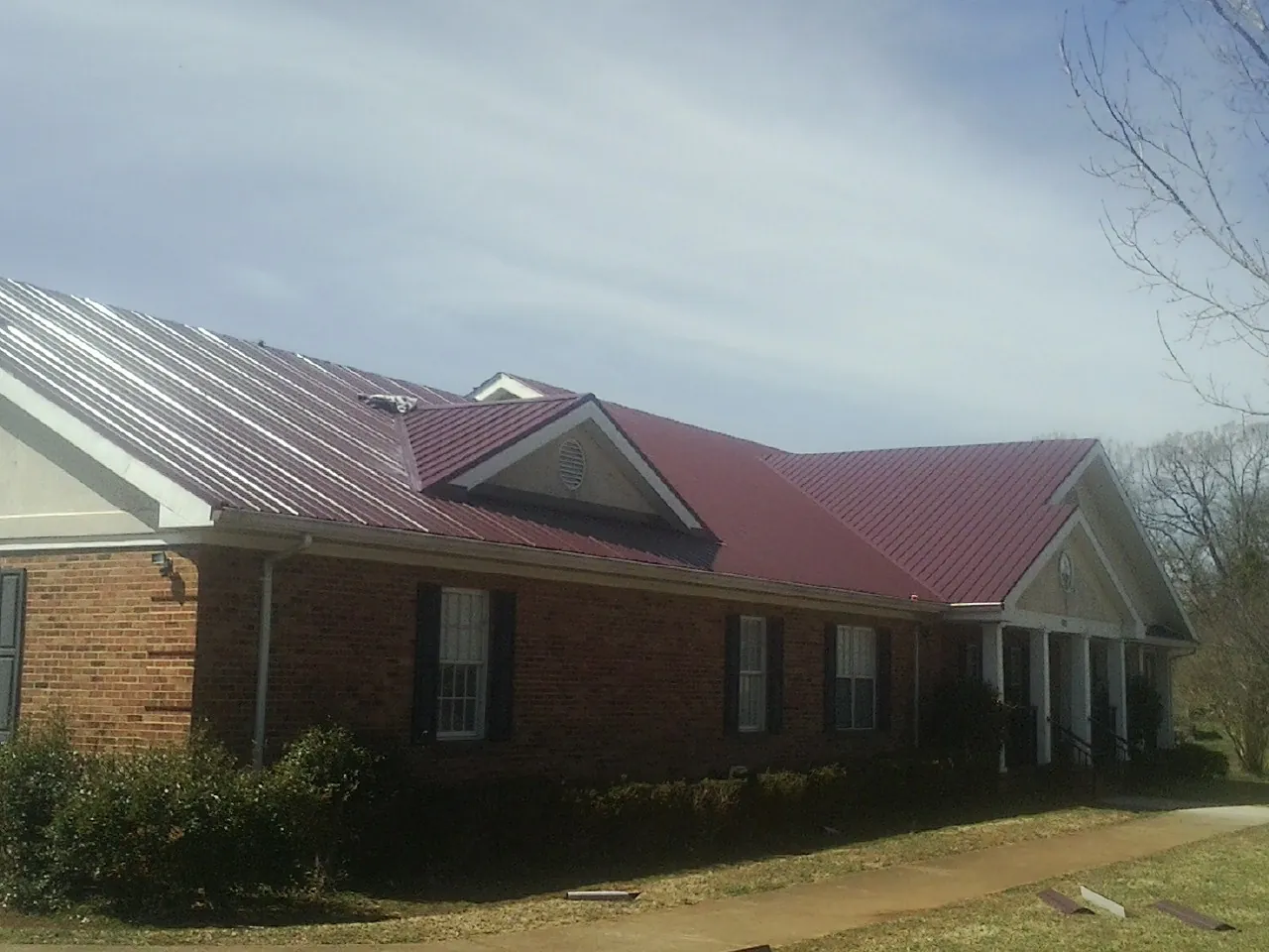 Red metal roof with gabled entries on a long brick building, from a Hail Damage Roof Repair job in Whiteland