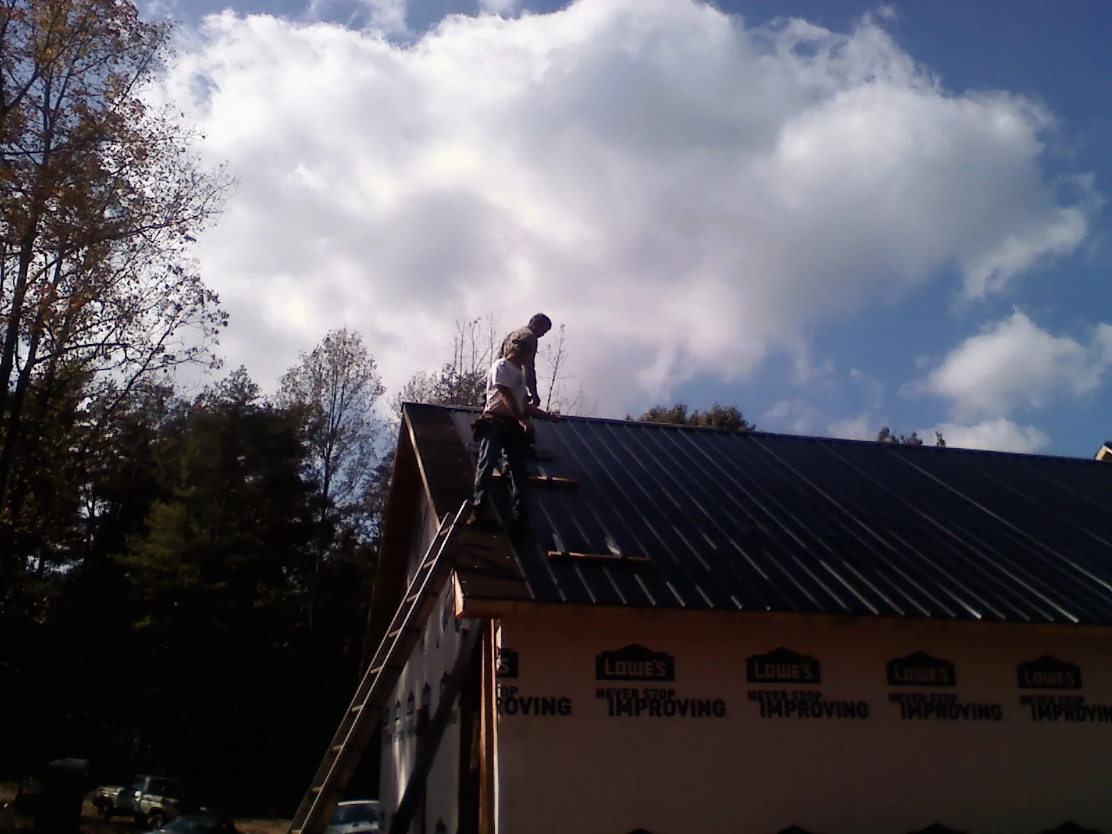 Roofer fastening dark metal panels high against a cloudy sky, from a Roof Inspection job in Whiteland