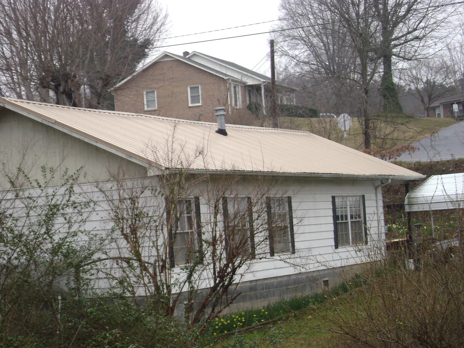 Tan metal roof on a white sided house set into a hillside — Commercial Roofing by Roofing Brothers in Whiteland