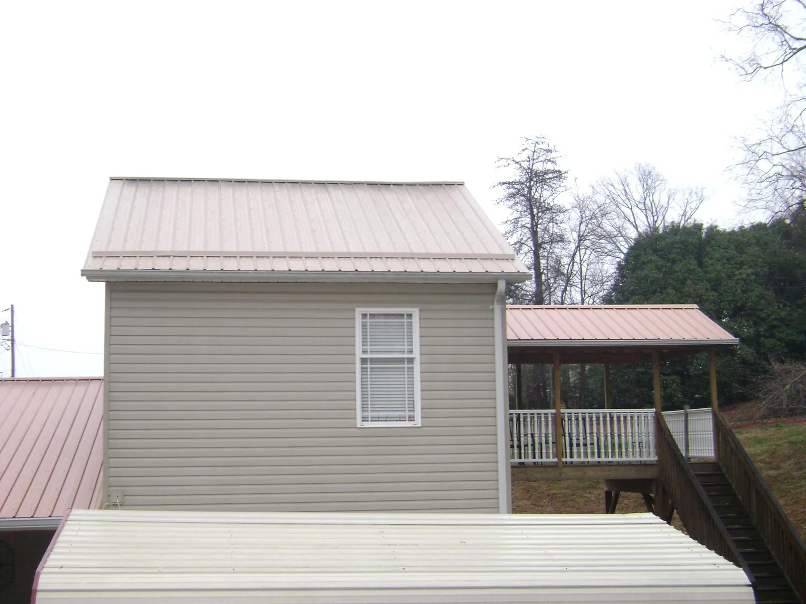 Tan metal roofs on a two story addition and attached porch, from a Roof Replacement job in Whiteland
